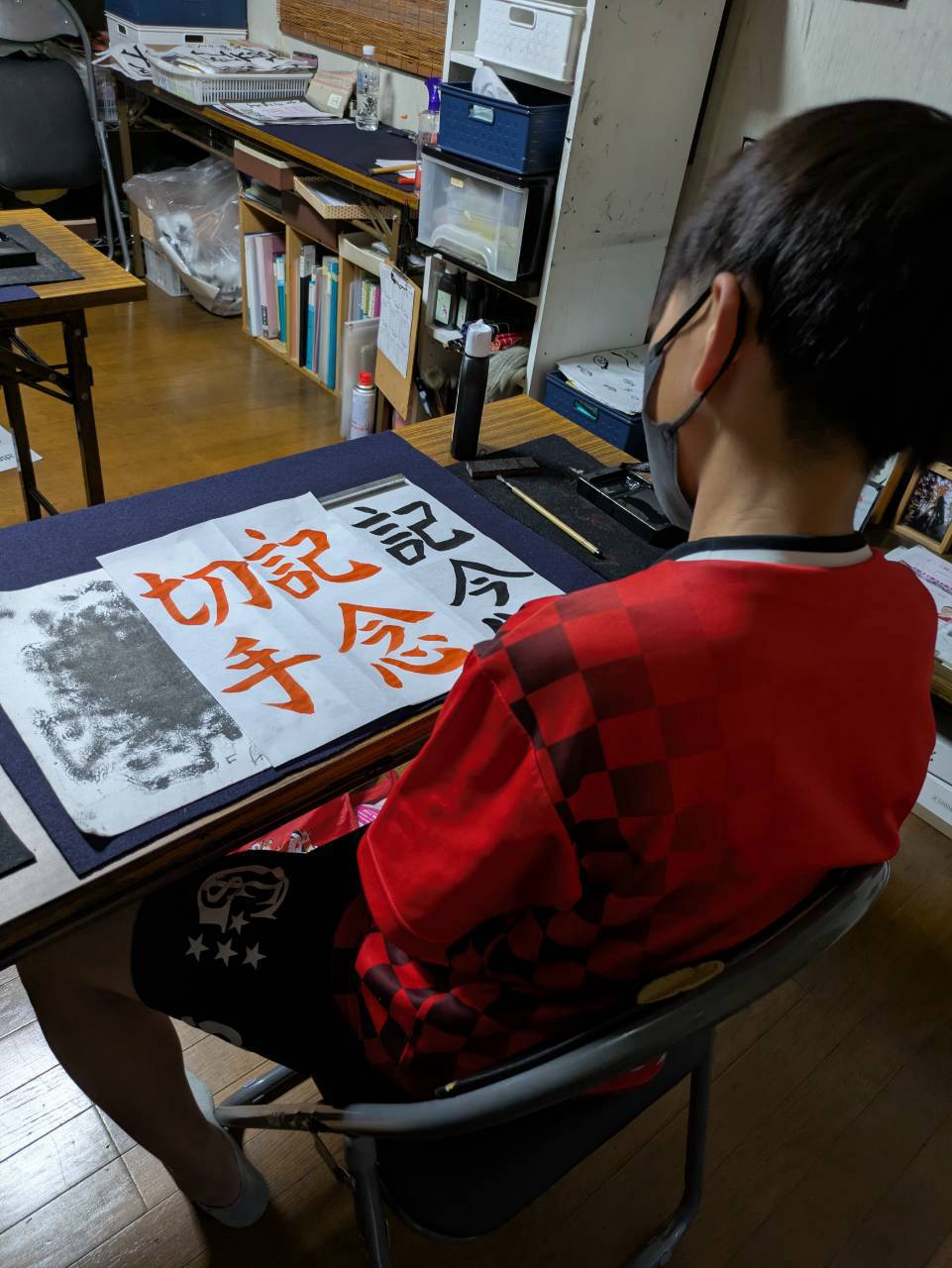 千詠書道 志木市教室で朱色のお手本を見ながら「記念切手」を毛筆で書く生徒さん